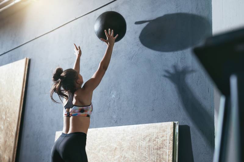 Frau wirft Medizinball im Fit-Life Fitnessstudio dynamisch an die Wand.